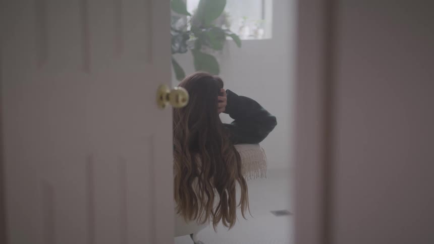 Door sits ajar revealing woman reclining with head propped on hand