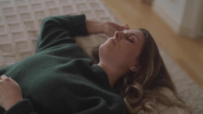 A woman in a green sweater sleeps atop on a bed