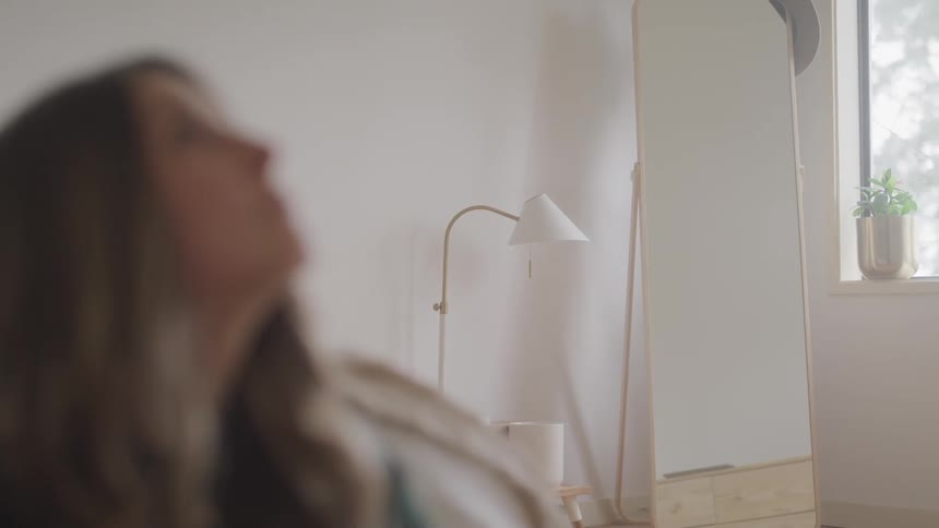 Out of focus woman sitting in the floor of a bedroom next to a full body mirror