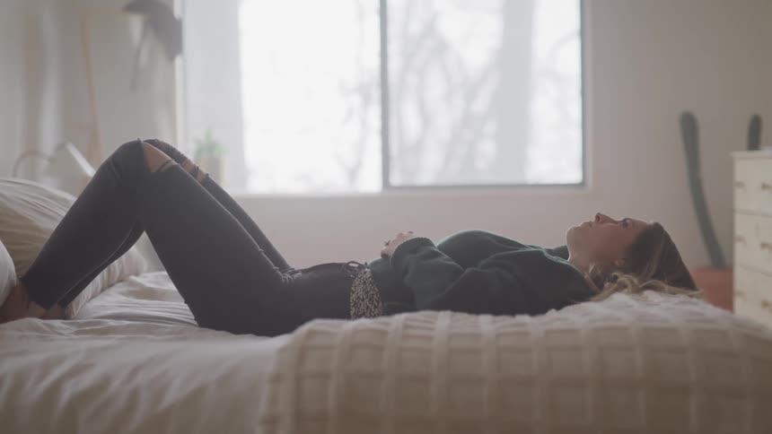 Woman lies on bed on her back looking up at the ceiling