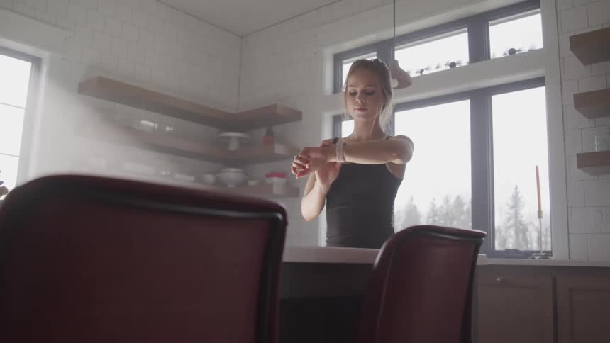 Woman stands in kitchen near island timing using her wristwatch
