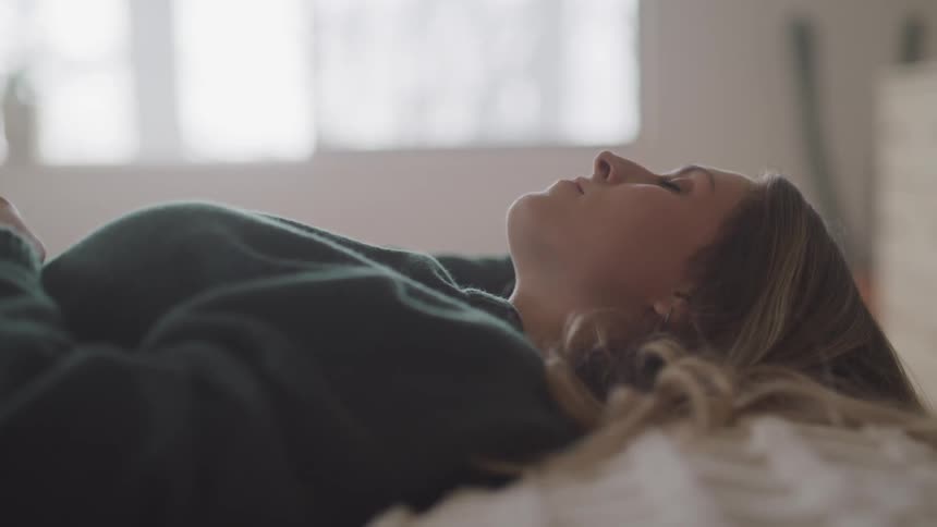 A woman lays on her bed looking to the ceiling during the daytime