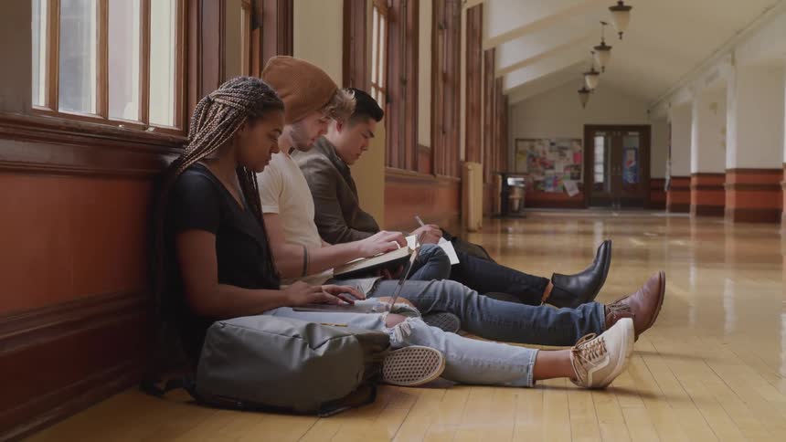 Three friends sit in a school hallway and read