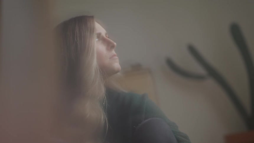 A woman sitting inside looking sad turns her head and looks to the side