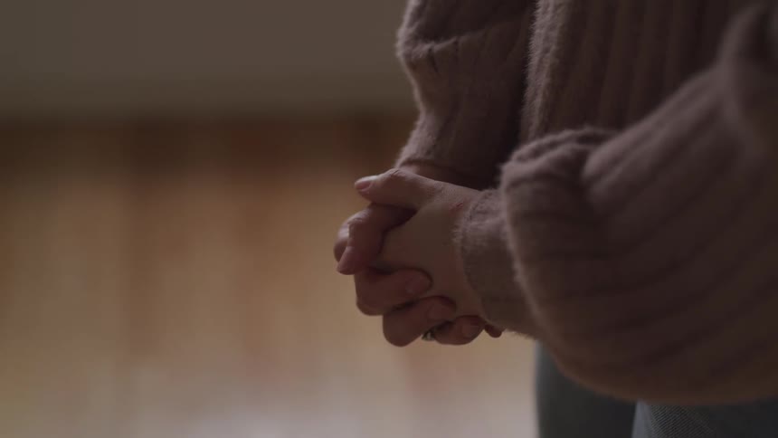 A woman with a ring and sweater and jeans standing with her hands folded