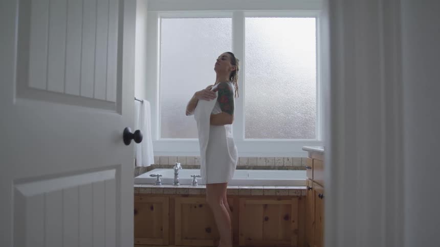 Tattooed woman with blonde hair covers her body with a white towel in the bathroom