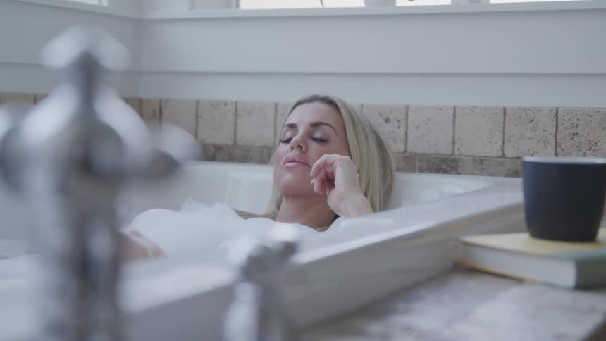 Woman with dirty blonde hair lies in a bathtub in the bathroom