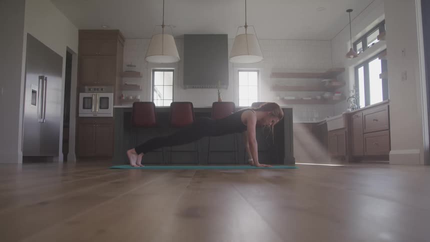 A woman does a push up on a yoga mat in her kitchen