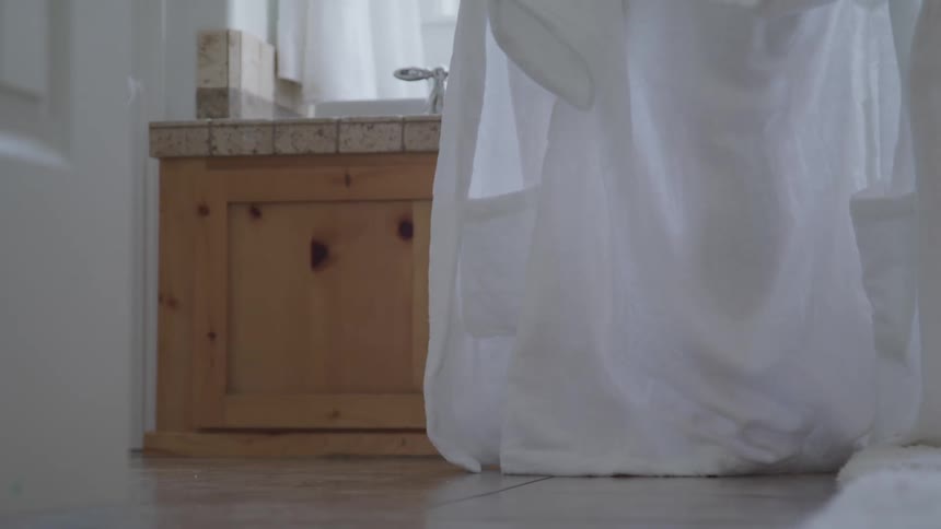 Woman takes off a white bathrobe to have a bath in the bathroom