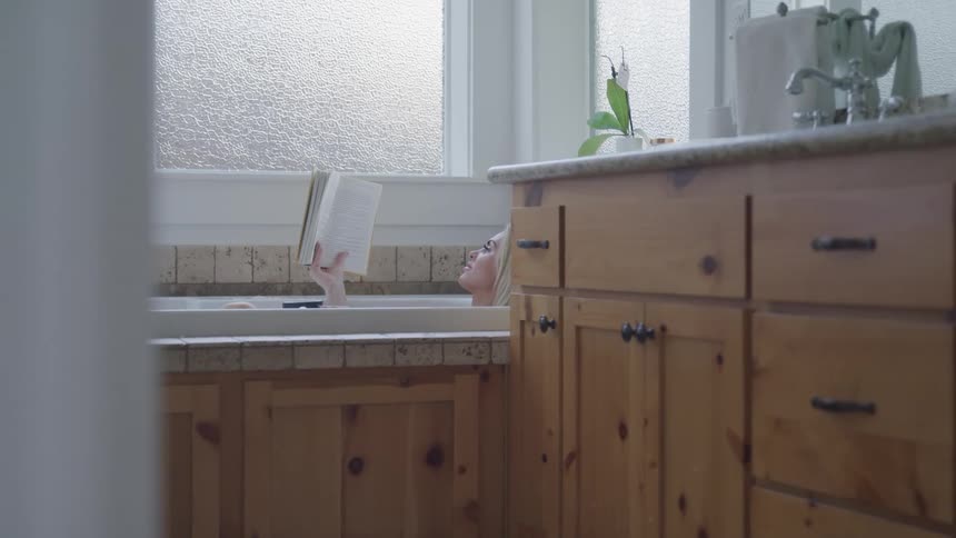 A woman is relaxing in a bathtub and reading a book