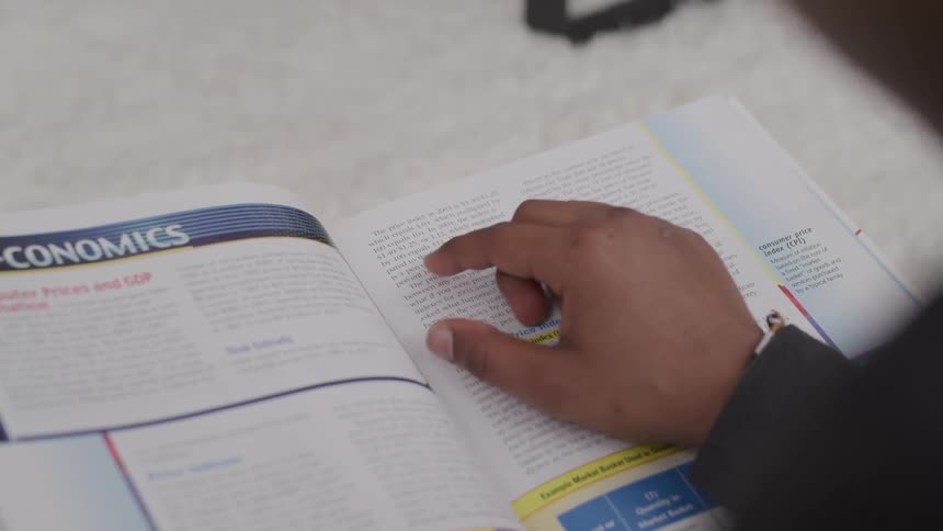 Finger on a black hand moves across the text in a book