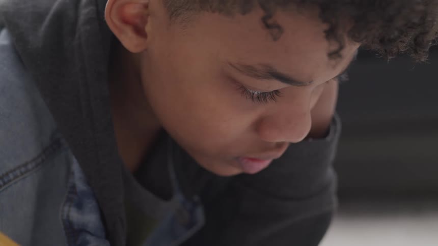 A boy with a jeans jacket and a hoodie holding a pencil and writing