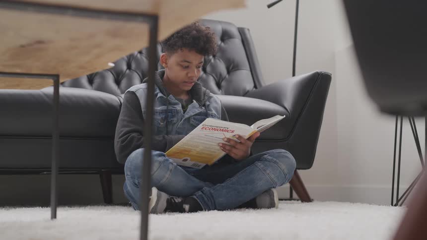 A boy sitting on the floor at home reads a book