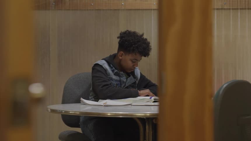 A teenage boy sits at a table and reads from a textbook