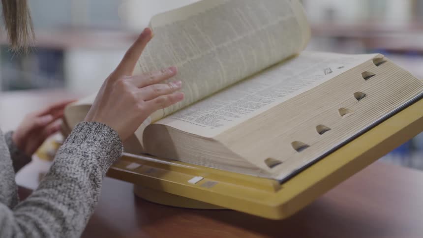 A teenage girl looks through a book in a library