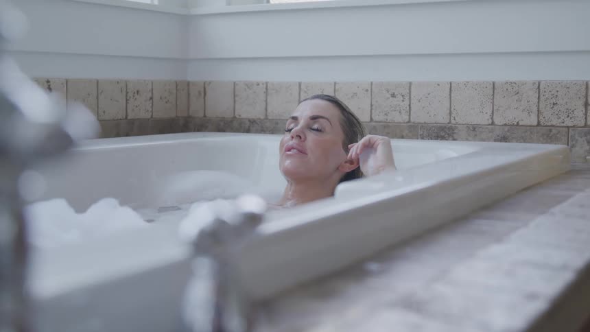 Woman with blonde hair lies in bathtub and closes her eyes
