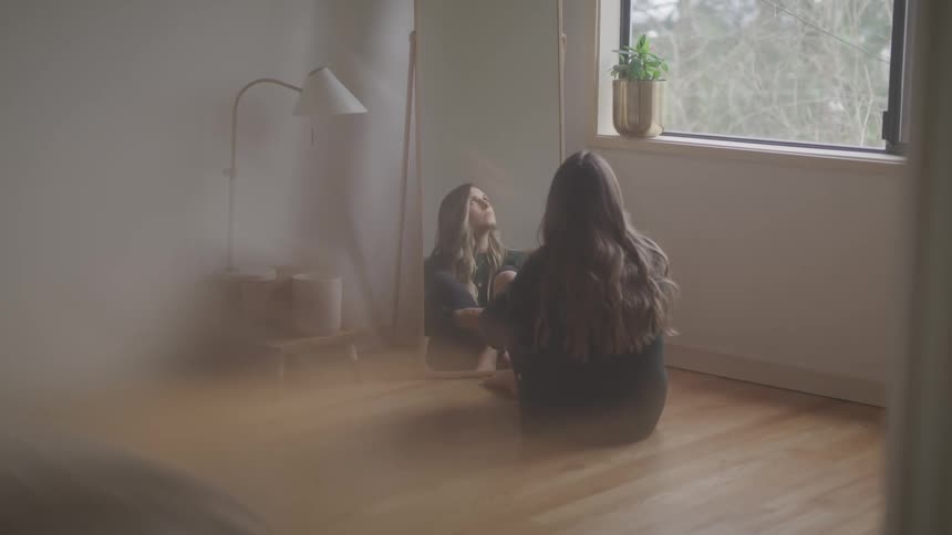 Long haired woman looks at the mirror while sitting in the floor of a room at home