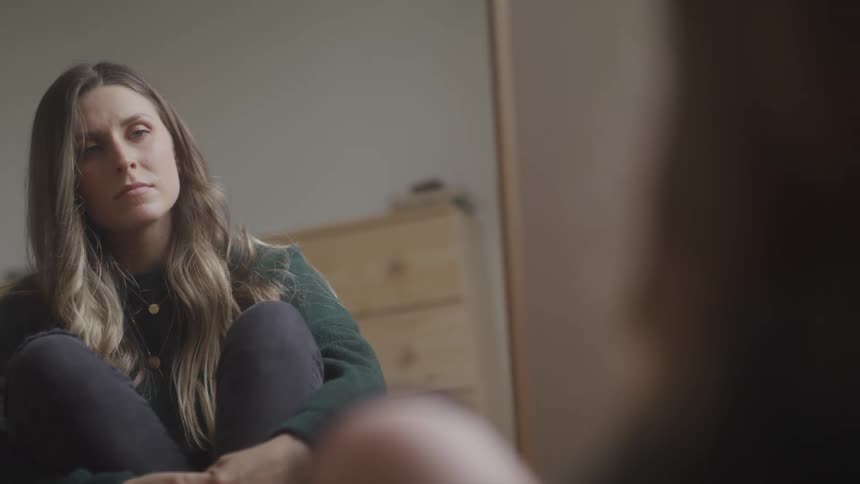 A woman sits on the floor at home and looks at herself in a mirror