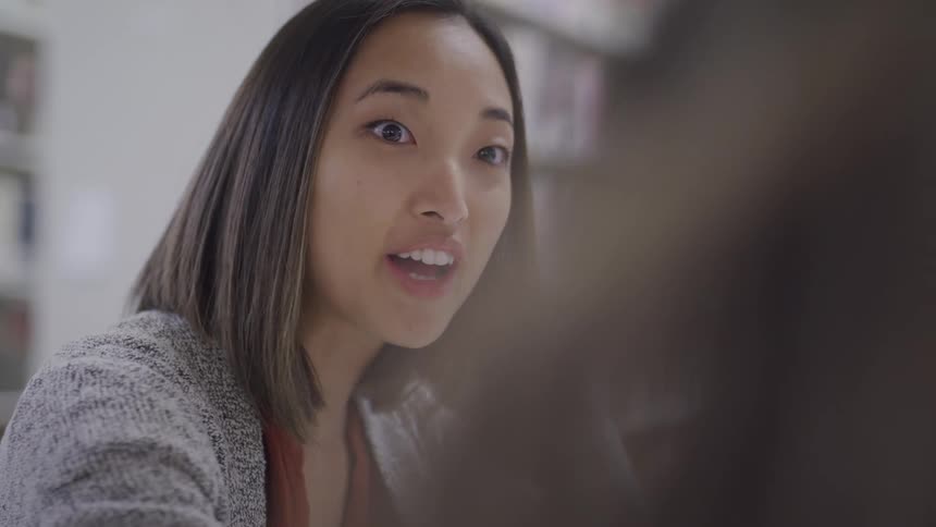 A young woman smiles and laughs while talking with a friend in the library