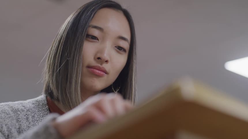 Asian girl with straight hair sitting at the desk studies in the library