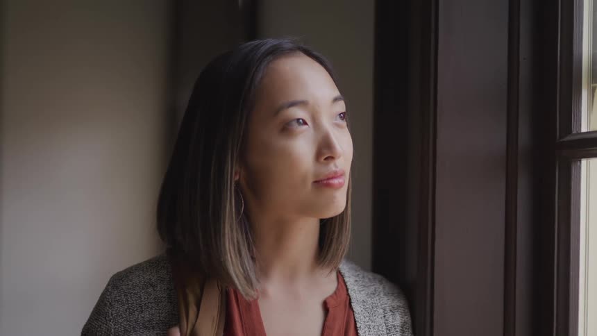A woman is standing indoors and looking out a window