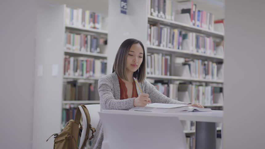 Teenage asian girl with straight hair sitting at the table writes down in the public library