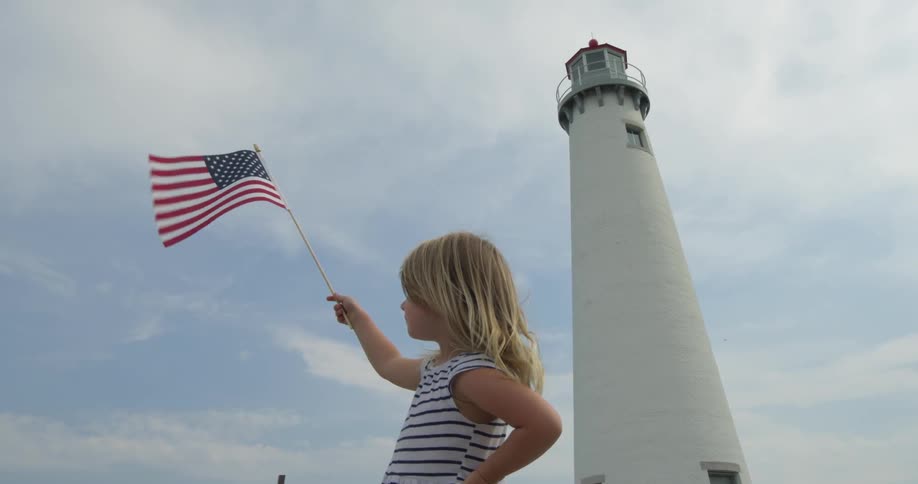 A girl holds an american flag with a lighthouse in the background