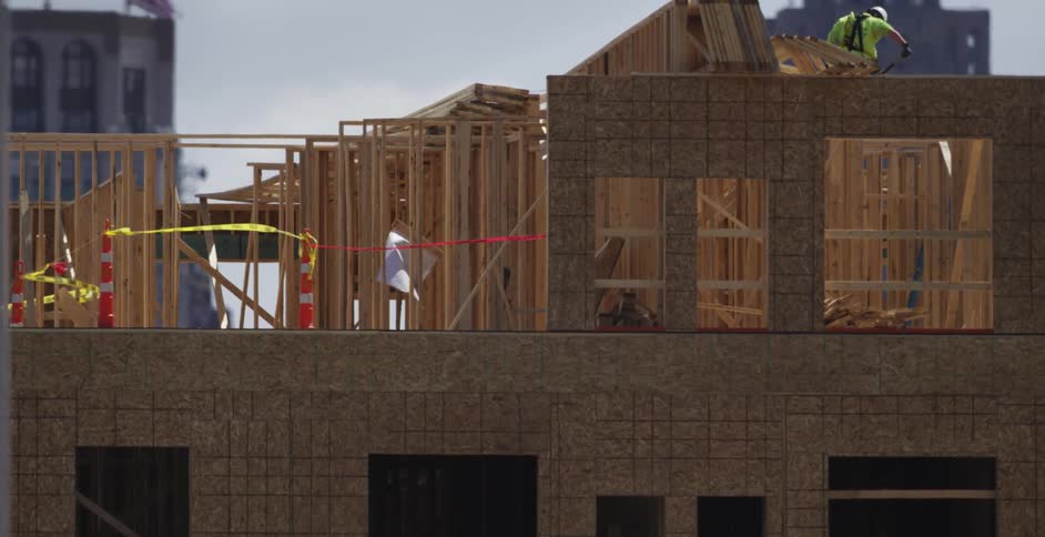 Construction workers stand on top of a building frame