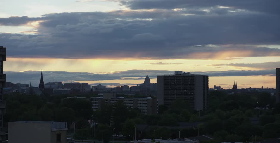 The sun sets over city buildings on a cloudy day