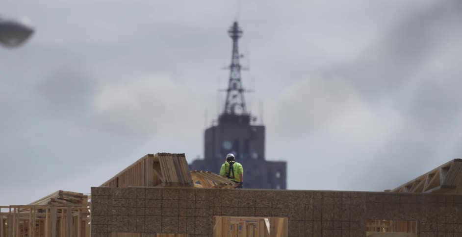 A construction worker stands on top of a framed building