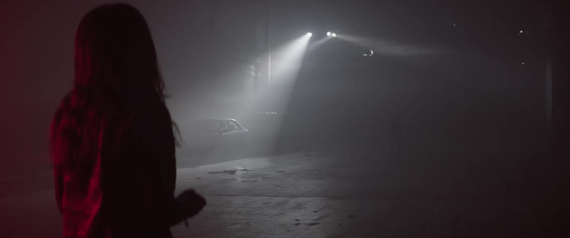 Three spotlights move over a street where one person is standing and another picks something up