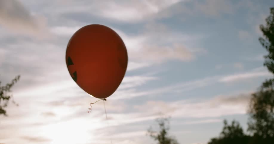 A jack-o-lantern balloon floats outside on a cloudy day