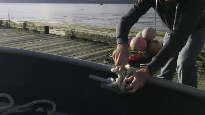 A man is tying a boat to the docks on a sunny day