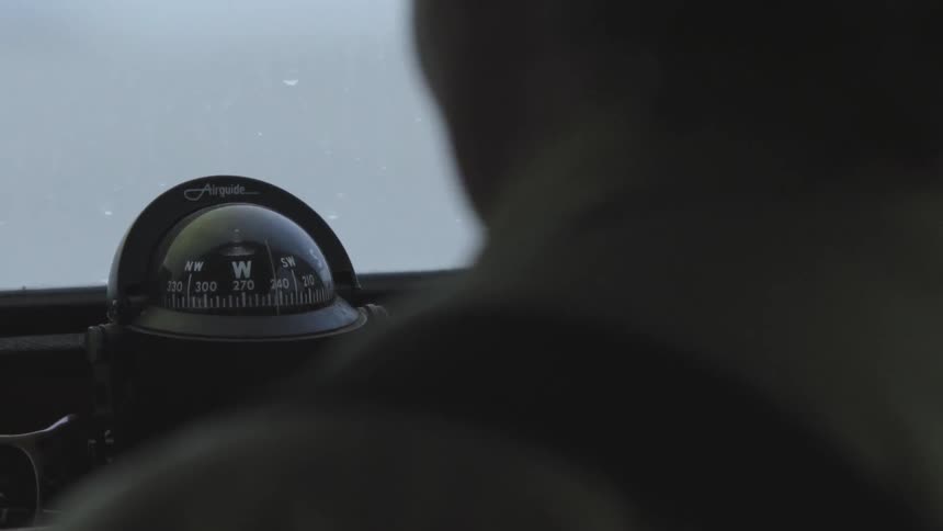 A compass is seen on a dashboard of what appears to be a plane