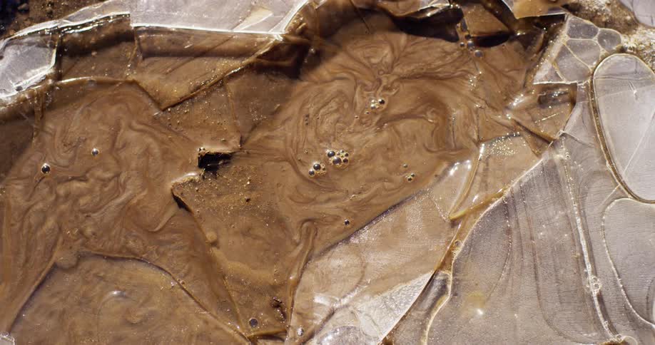 A boot steps on a frozen mud puddle