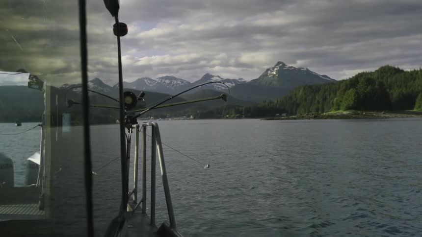 A man exits the cabin of a ship with mountains in the distance
