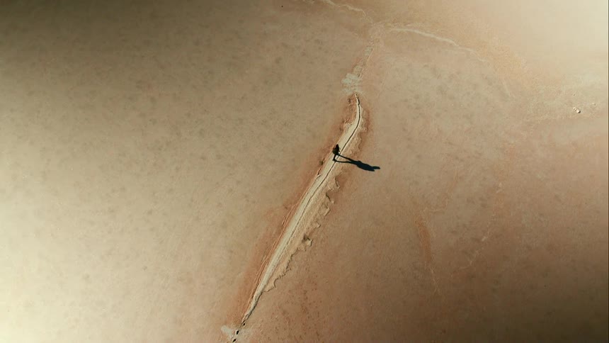 Aerial rise above a woman walking through desert vastness