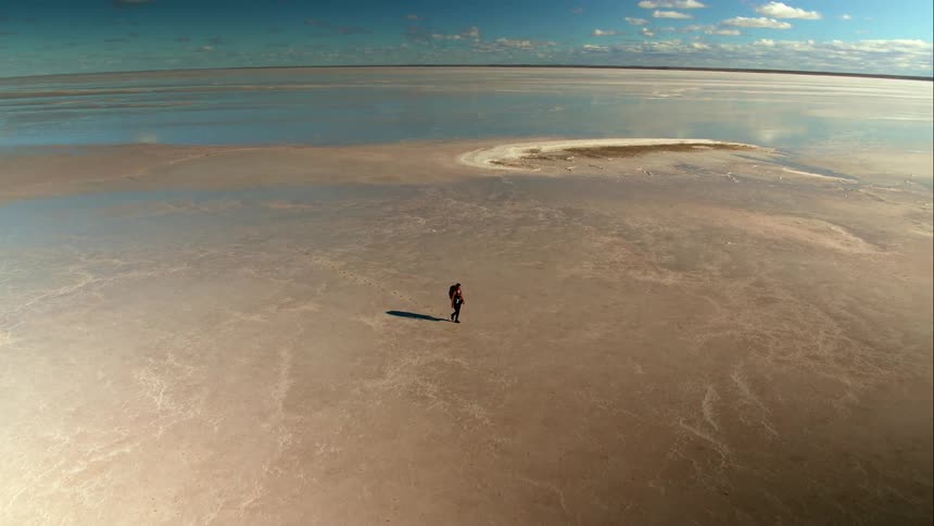 Aerial of a woman walking through endless reflective salt flats