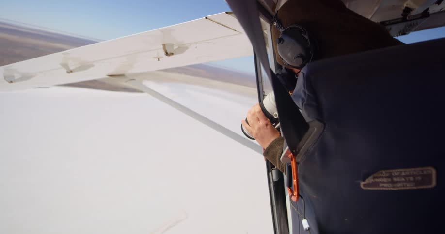 A photographer uses a camera to take pictures of the landscape from an aircraft