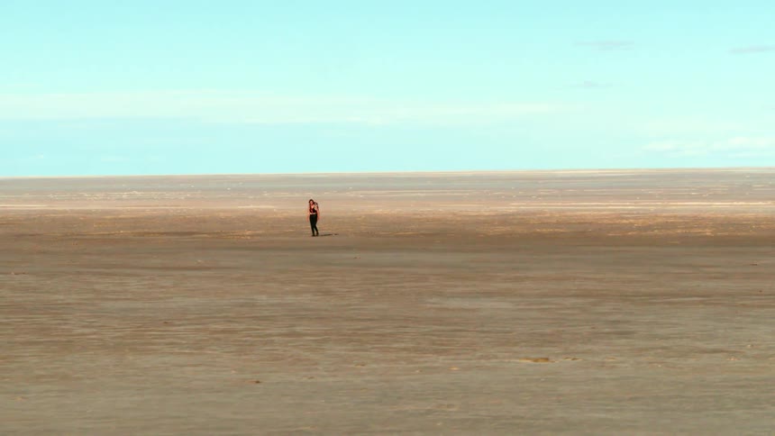 Aerial pulling away from a woman walking in a huge desert