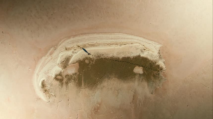 Man walks across arid sandy plain leaving footsteps in the ground