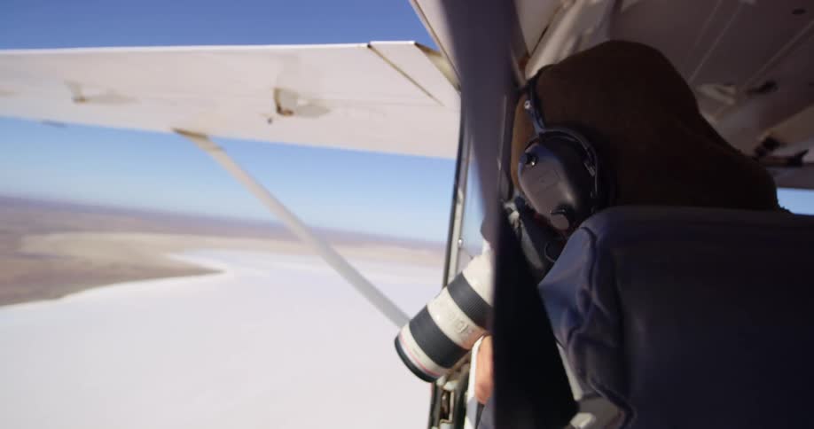 A woman takes photos of a desert land from an airplane