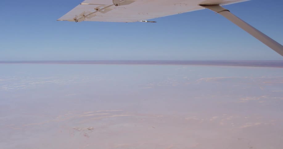 A plane flies above salt flats