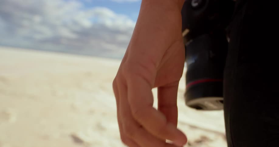 A photographer walks through the desert with a camera slung over her shoulder