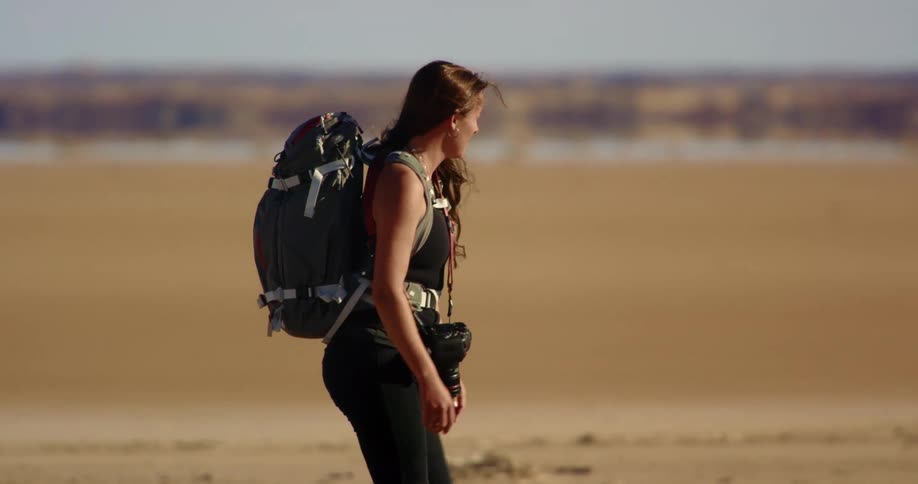 Photographer wearing a backpack walks through a desert carrying a camera