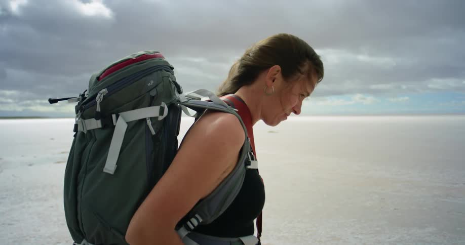 A woman wearing a large backpack hikes through the desert in the wind