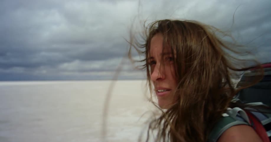 A woman hikes alone through a barren desert on a windy day with a large backpack