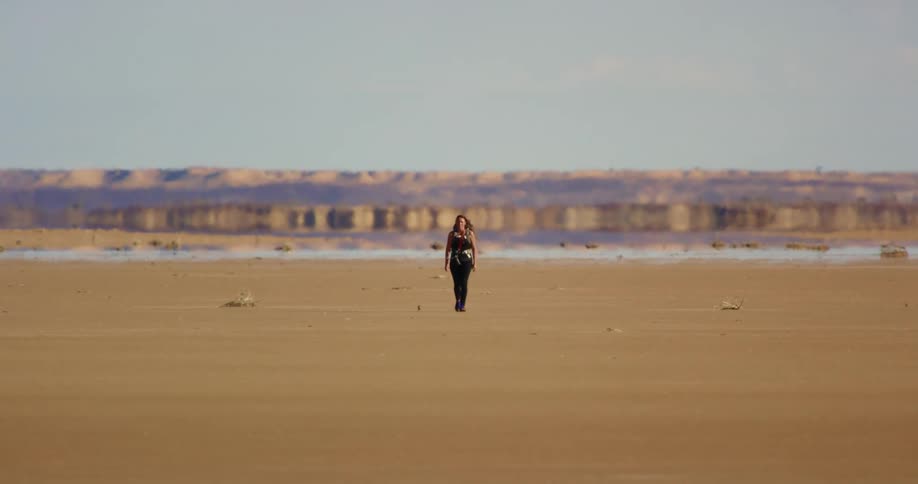 A woman walking across a shimmering desert towards us