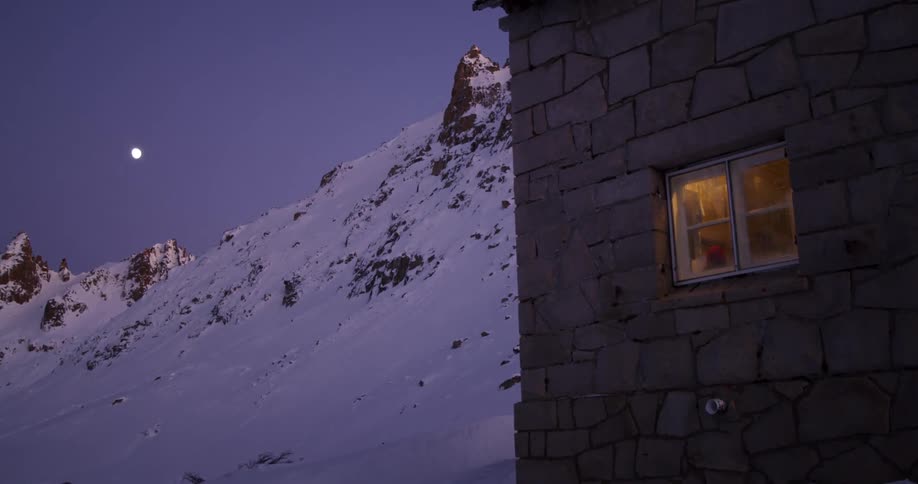 Silhouettes of people can be seen in a building next to a snow covered mountain slope