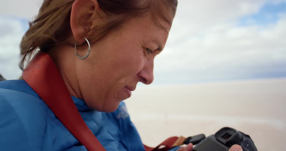 A photographer squints as she takes photos in a desert on a windy day